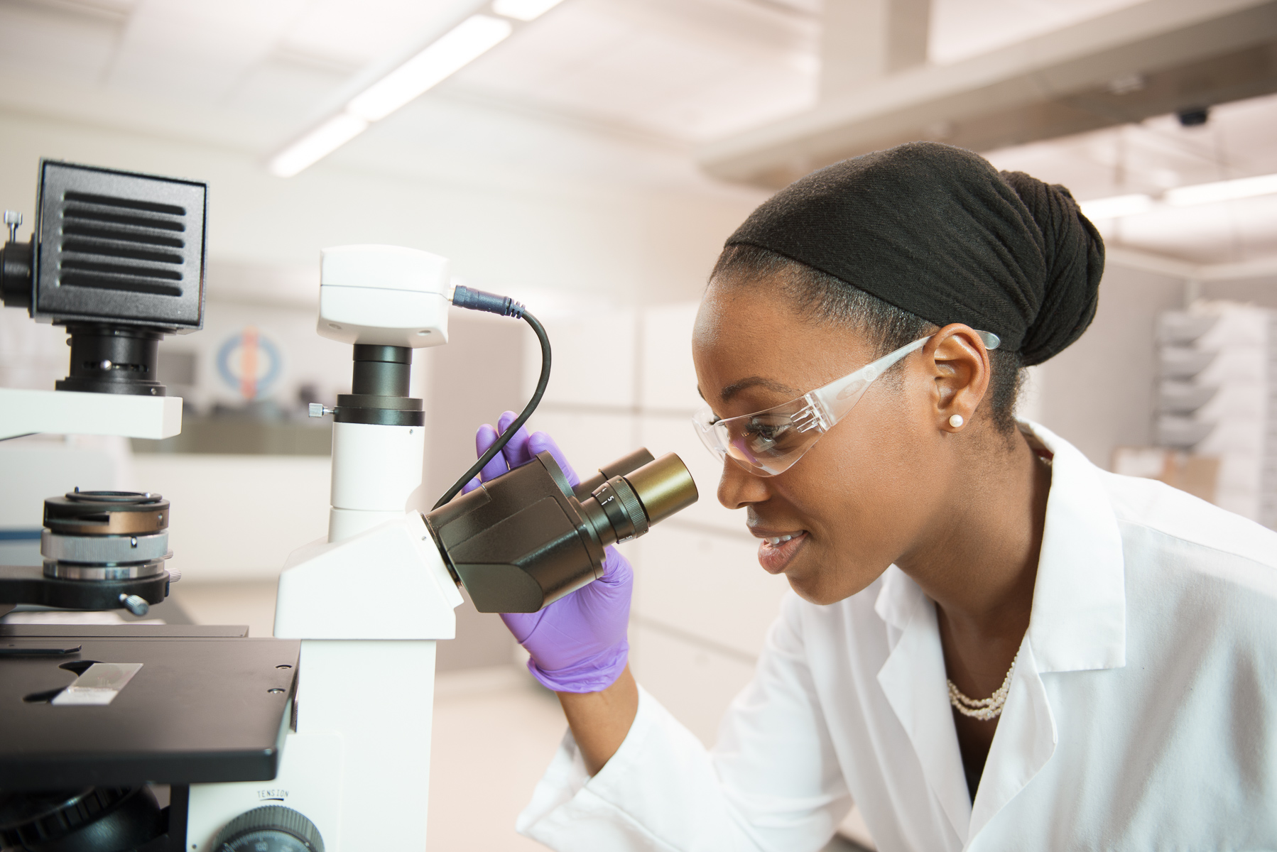 African-American female biotech scientist uses microscope