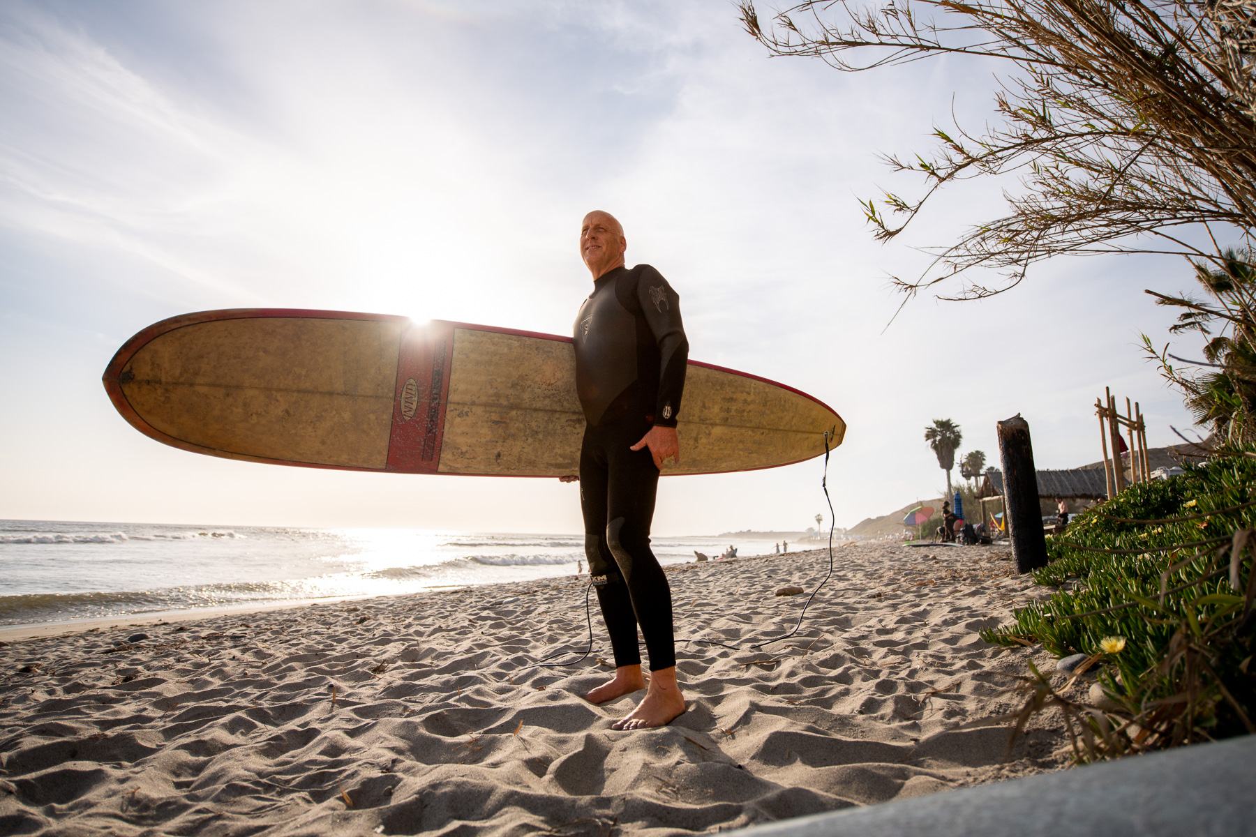 Senior surfer stands with longboard on beach